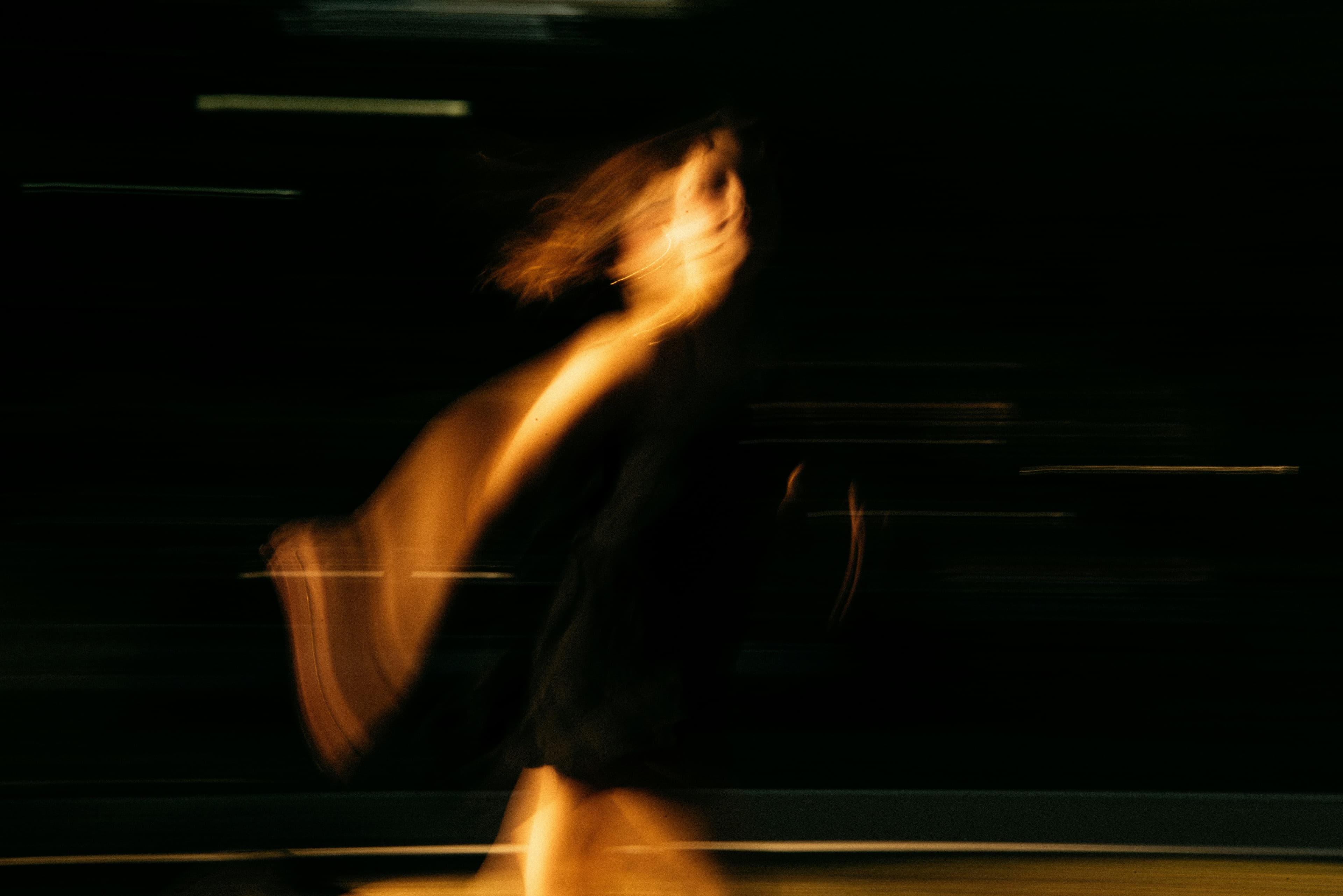 Blurred image of a person in motion against a dark background, creating a dynamic and abstract effect with warm lighting.